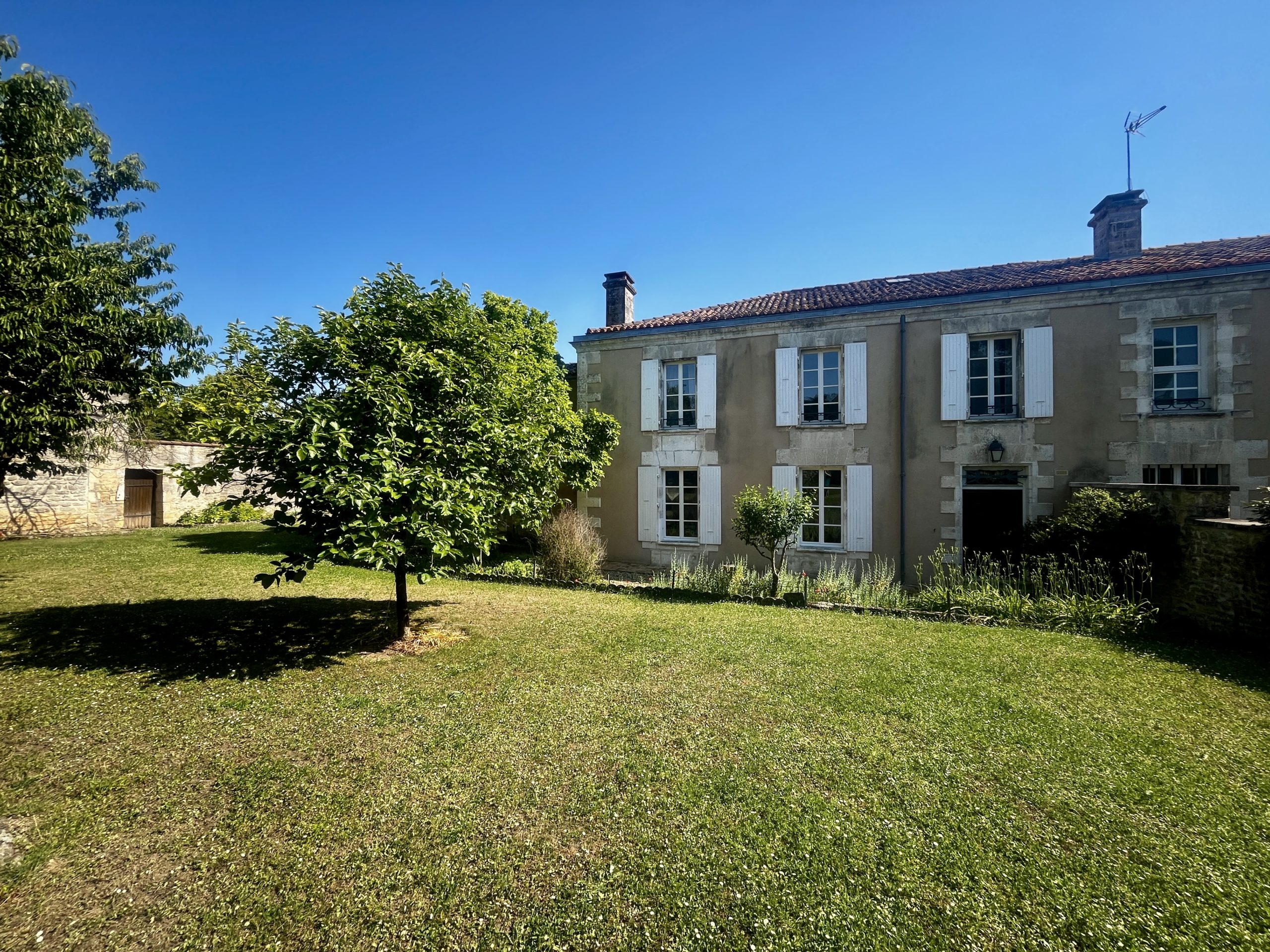 Maison ancienne aux volets blancs dans un jardin ensoleillé